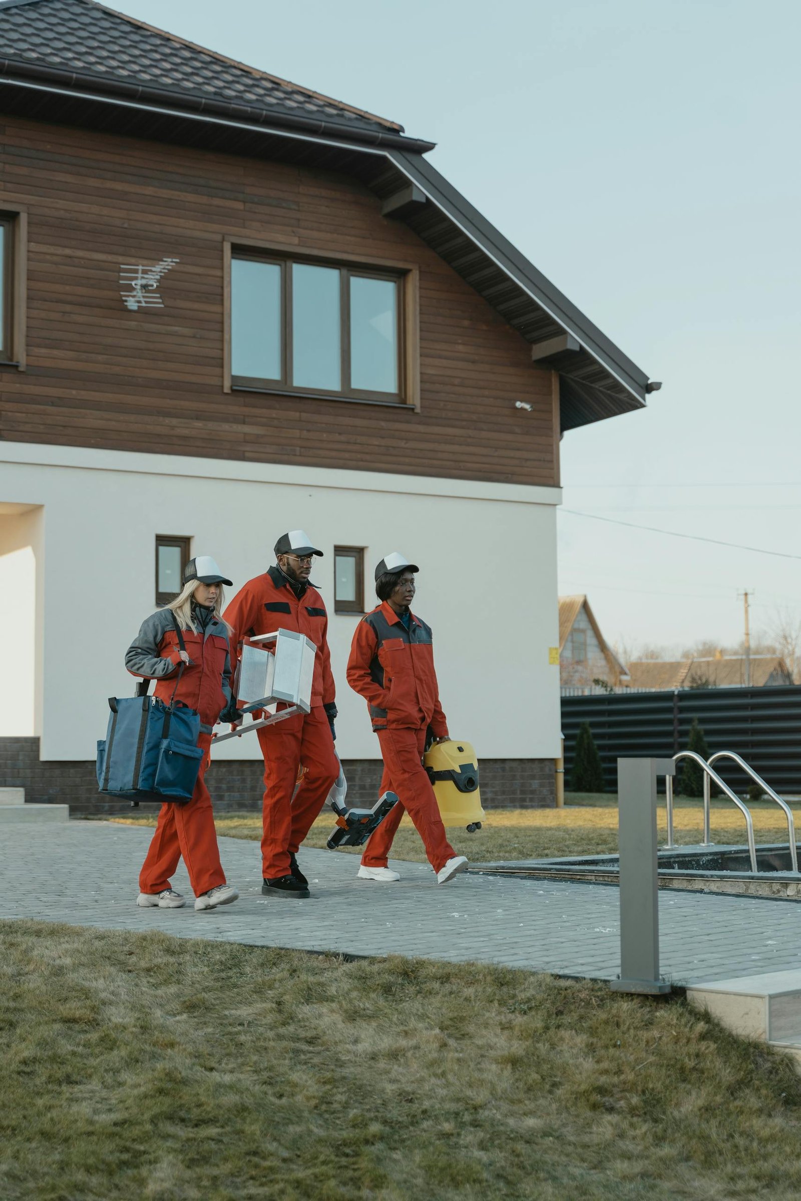 Team in red uniforms carrying cleaning supplies towards a modern home.